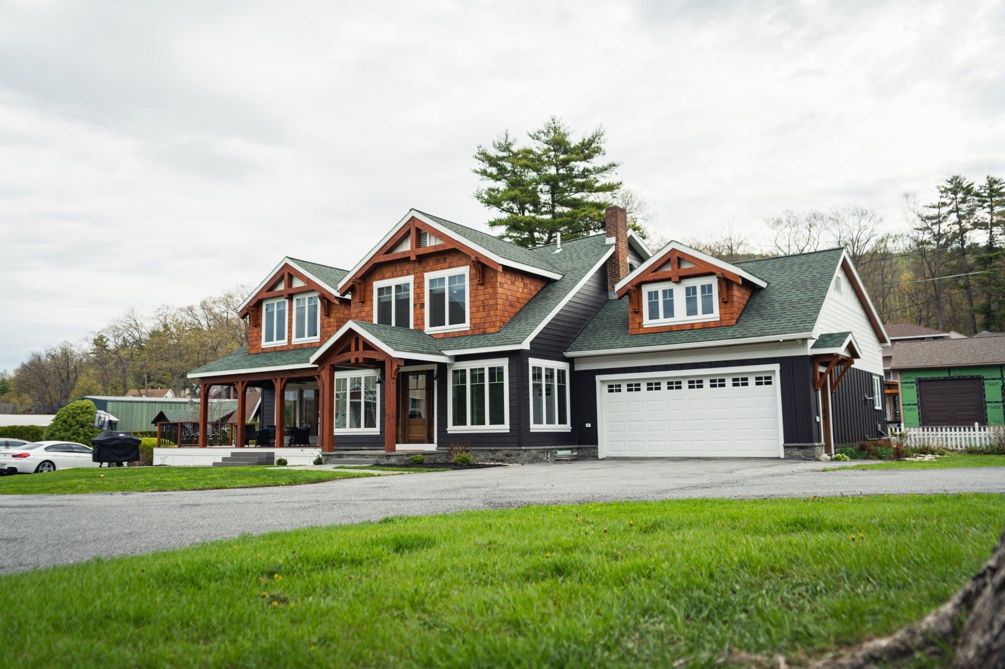 Front exterior of Rose Point Lodge — a timber-frame lake house with a green roof, cedar shingles, and a covered porch.